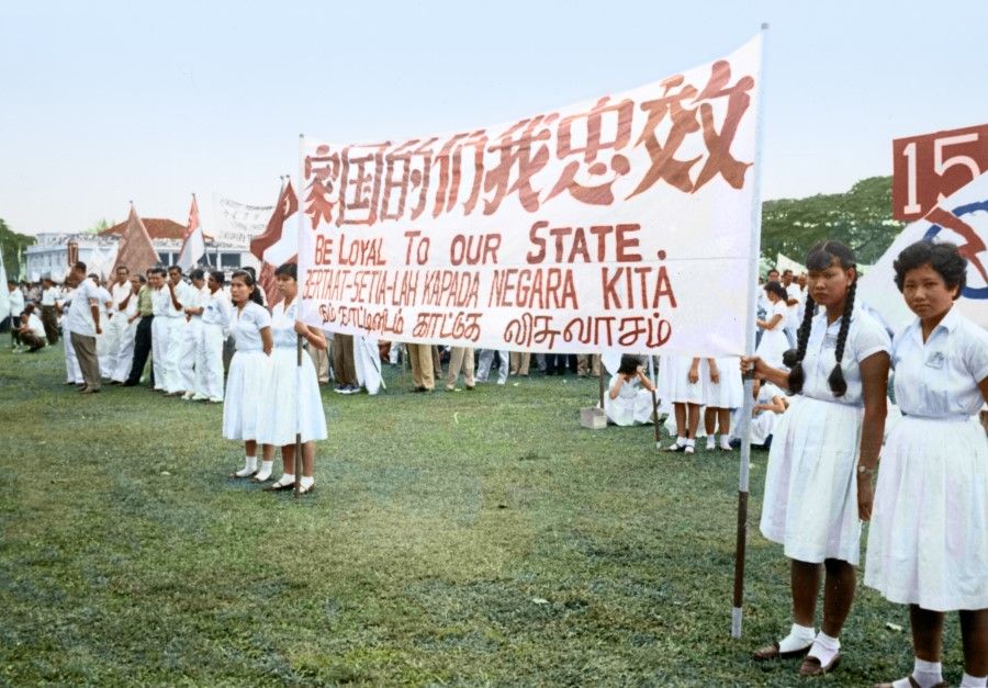 Singapore's National Day celebration, 1968. The students on the field are holding a banner with the slogan "Be Loyal to Our State" in four languages.