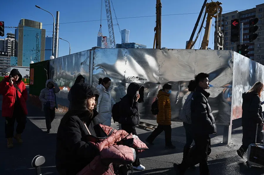 People walk past a construction site in Beijing, China, on 8 December 2024. (Greg Baker/AFP)