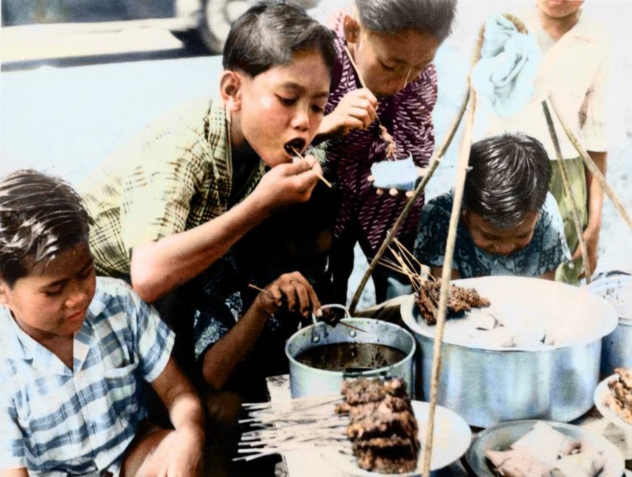 Children enjoy satay at a stall in a market, 1960s. Satay is a typical Malay dish that usually features meats like beef and chicken and mutton.