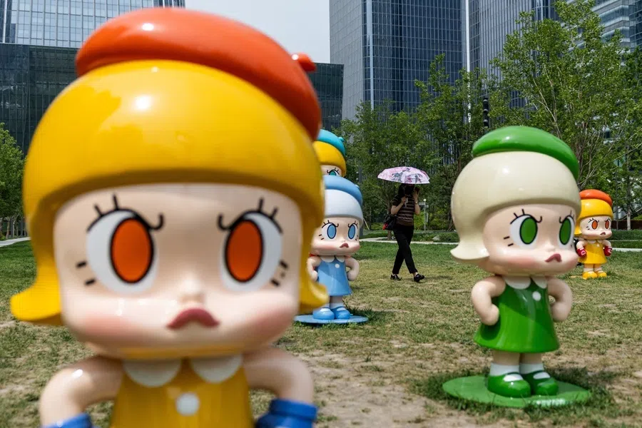 A woman carrying an umbrella to protect from the sun walks next to figures of Pop Mart’s character Molly on a hot day in Beijing, China, 2 June 2026.