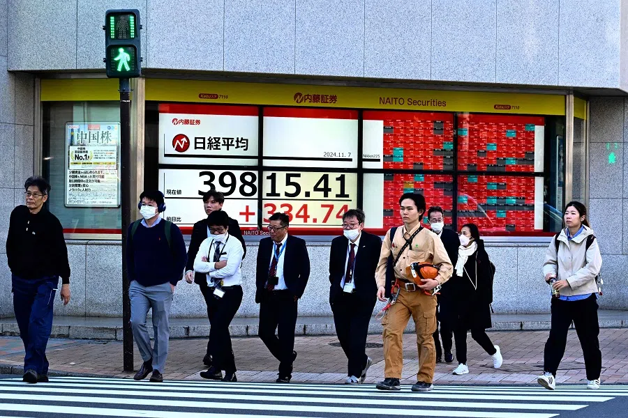 People walk past an electronic board displaying the numbers on the Tokyo Stock Exchange in Tokyo on 7 November 2024. (Yuichi Yamazaki/AFP)