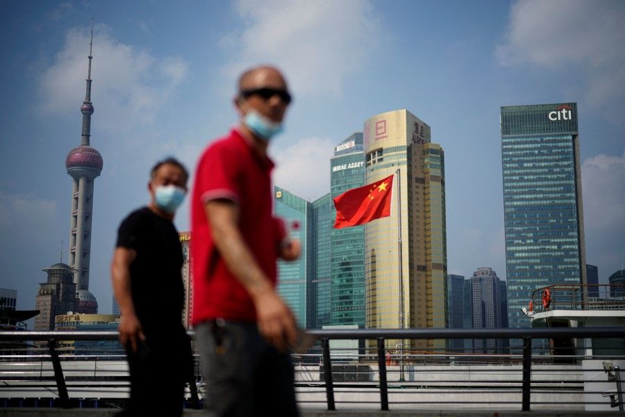 People wearing face masks following the Covid-19 outbreak walk past a Chinese flag in Shanghai, China, 2 August 2022. (Aly Song/Reuters)