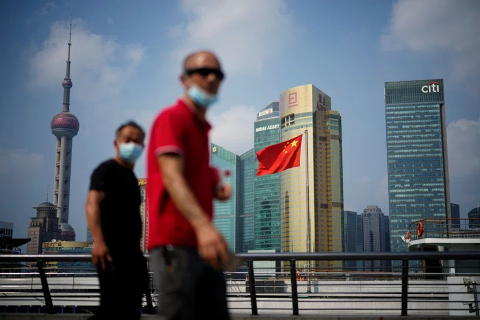 People wearing face masks following the Covid-19 outbreak walk past a Chinese flag in Shanghai, China, 2 August 2022. (Aly Song/Reuters)