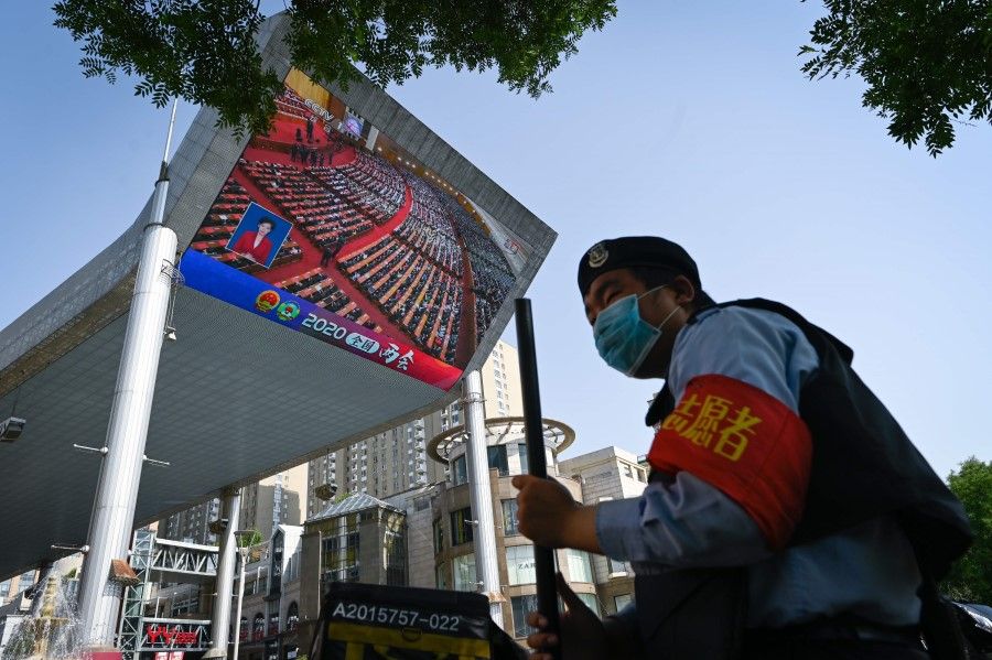 A security volunteer stands in front of an outdoor screen showing live coverage of the closing session of the National People's Congress (NPC) in Beijing, 28 May 2020. (Wang Zhao/AFP)
