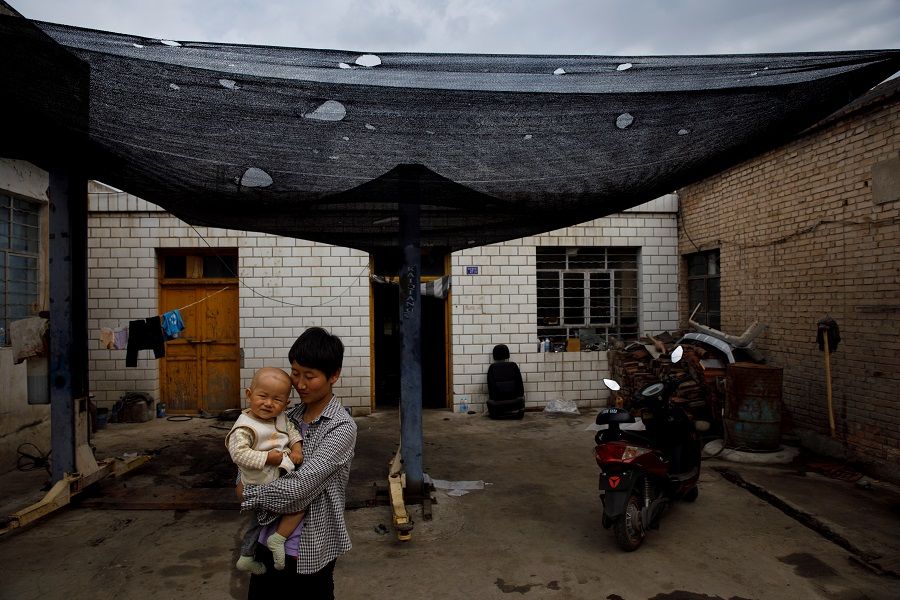 A woman holding her child stands in front of her family's car repair shop opposite the decommissioned Liancheng coal-fired power plant in Heqiao village, Yongdeng county, Gansu province, China, 16 September 2020. (Thomas Peter/Reuters)