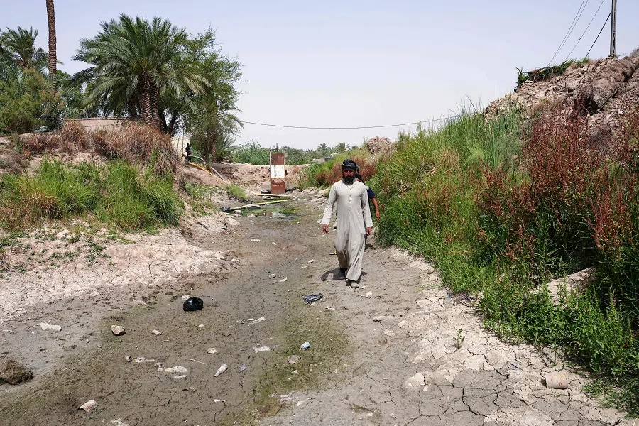 People walk along a dried up stream in Mishkhab, in Iraq’s Najaf on 24 May 2025, where years of drought have negatively affected the fauna and flora of the region. (Qassem al-Kaabi/AFP)