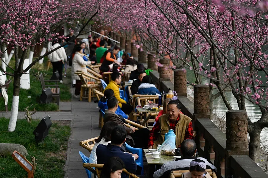 People sit along a river at a park in Chengdu, China's Sichuan province on 19 February 2024. (Wang Zhao/AFP)