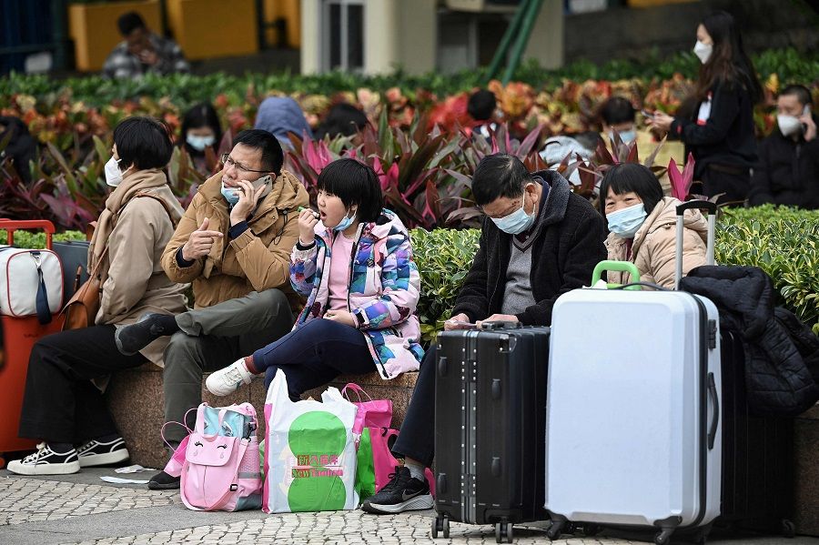 This photo taken on 17 January 2023 shows tourists sitting on a public bench with their suitcases in Macau, China. (Peter Parks/AFP)