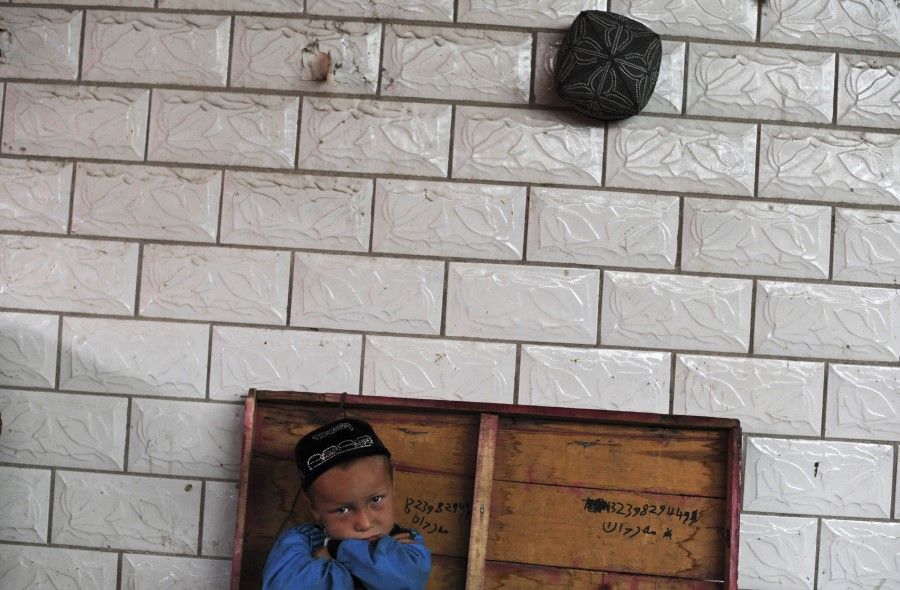 A boy from the Uighur ethnic group sits in front of a wall, with an Islamic cap hung on it, in Aksu, Xinjiang Uyghur Autonomous Region, 10 June 2012. (Stringer/Reuters)
