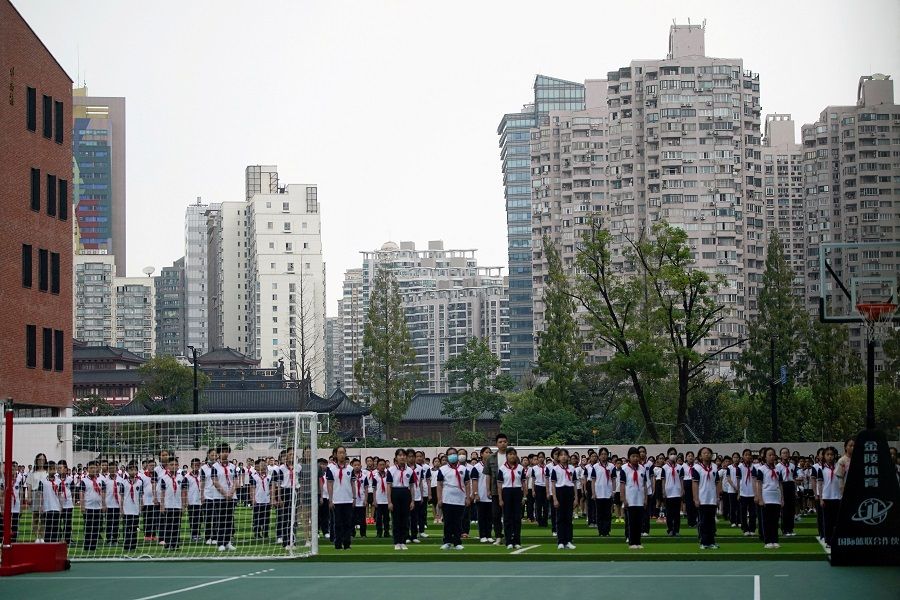Students stand at a school during a flag-lowering ceremony on the first day of the new academic year in Shanghai, China, 1 September 2021. (Aly Song/Reuters)
