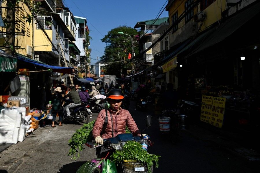 A woman carries vegetables on her scooter along a street in the old quarters of Hanoi on 30 November 2020. (Manan Vatsyayana/AFP)