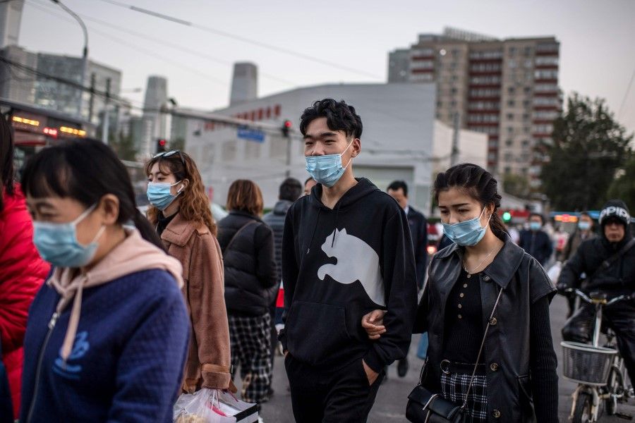 People wearing face masks as a preventive measure against the Covid-19 coronavirus cross a street during rush hour in Beijing on 21 October 2020. (Nicolas Asfouri/AFP)