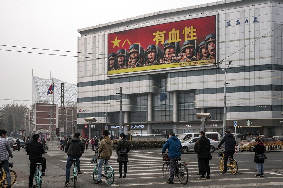 Pedestrians and cyclists stand in front of a screen showing an advertisement for the People's Liberation Army (PLA) in Beijing, China, on 5 March 2021. (Qilai Shen/Bloomberg)