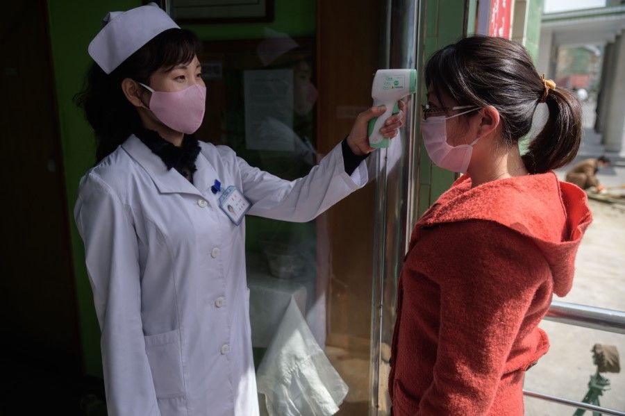 A health worker takes the temperature of a woman amid concerns over the Covid-19 coronavirus, at an entrance of the Pyongchon District People's Hospital in Pyongyang, 1 April 2020. (Kim Won Jin/AFP)