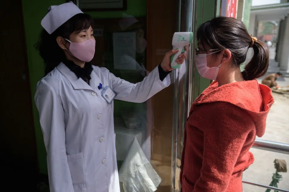 A health worker takes the temperature of a woman amid concerns over the Covid-19 coronavirus, at an entrance of the Pyongchon District People's Hospital in Pyongyang, 1 April 2020. (Kim Won Jin/AFP)