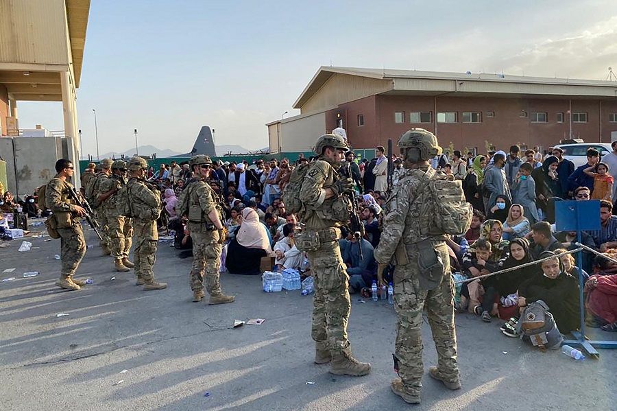 US soldiers stand guard as Afghan people wait to board a US military aircraft to leave Afghanistan, at the military airport in Kabul, Afghanistan, on 19 August 2021. (Shakib Rahmani/AFP)