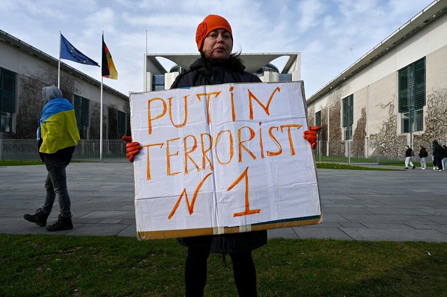 A demonstrator poses in front of the German Chancellery in Berlin, Germany, on 24 February 2022 with a placard, following Russia's military operation in Ukraine. (John Macdougall/AFP)