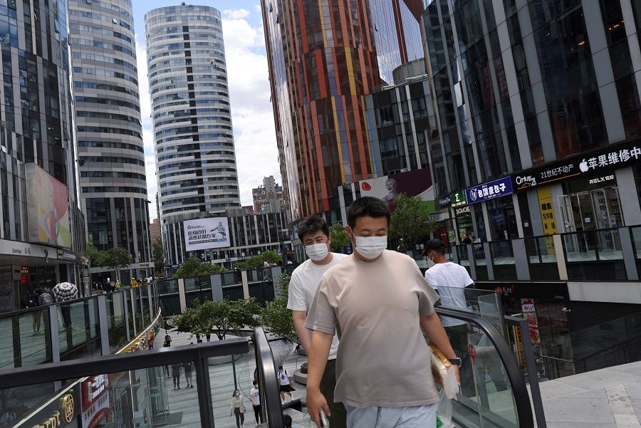 People walk past a shopping and office complex in Beijing, China, 6 June 2022. (Tingshu Wang/Reuters)