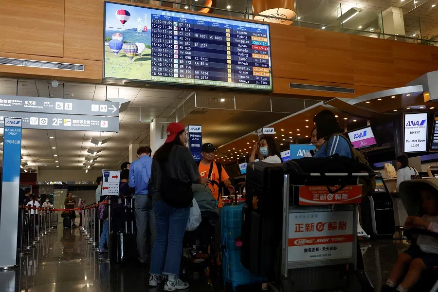 People wait in line near a screen displaying flight information at the international departures hall of the Taipei Songshan Airport in Taipei, Taiwan, on 24 July 2024. (Carlos Garcia Rawlins/Reuters)