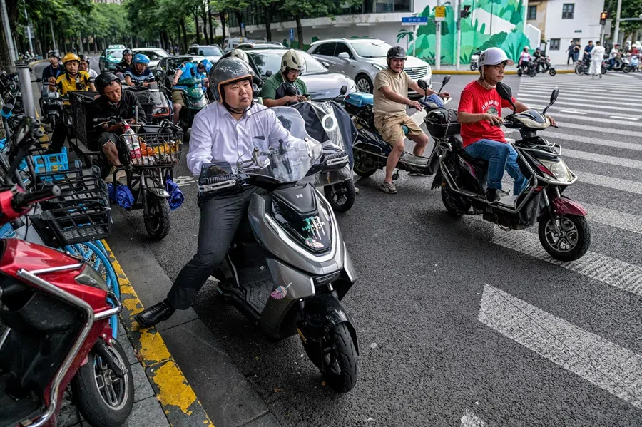 People riding scooters wait to cross a street in the Jing’an district in Shanghai on 24 June 2025. (Hector Retamal/AFP)
