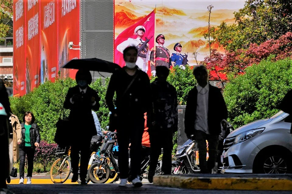 People cross a street in front of a large propaganda poster in Shanghai, China, 10 April 2023. (Aly Song/Reuters)