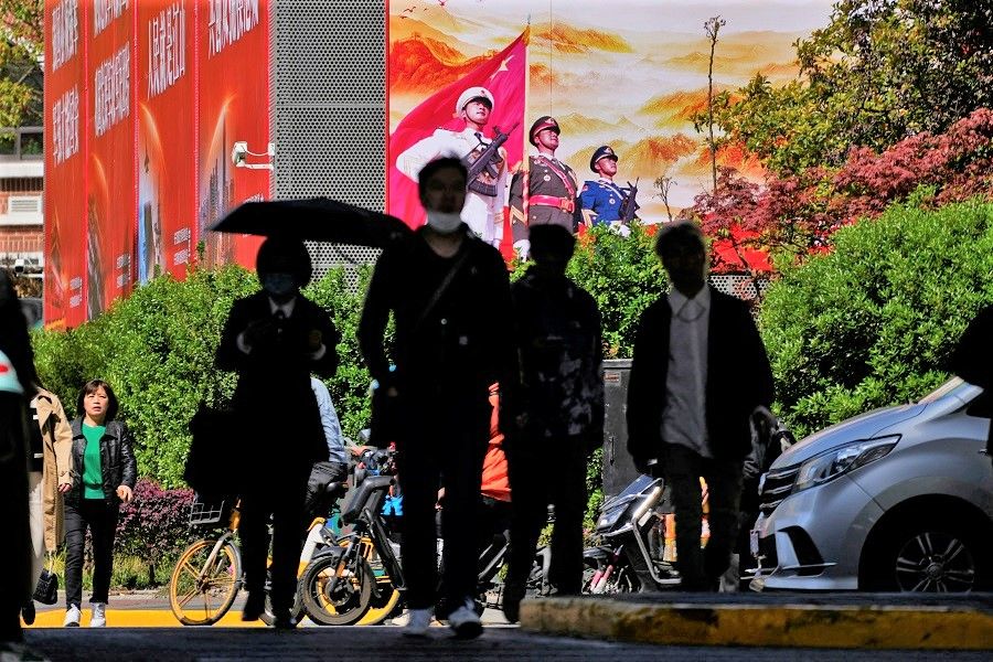 People cross a street in front of a large propaganda poster in Shanghai, China, 10 April 2023. (Aly Song/Reuters)