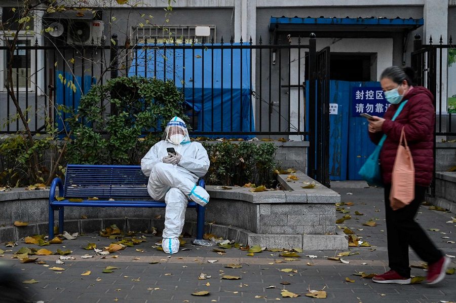 A man wears personal protective equipment as he sits outside a residential building under lockdown due to Covid-19 restrictions in Beijing, China, on 22 November 2022. (Jade Gao/AFP)
