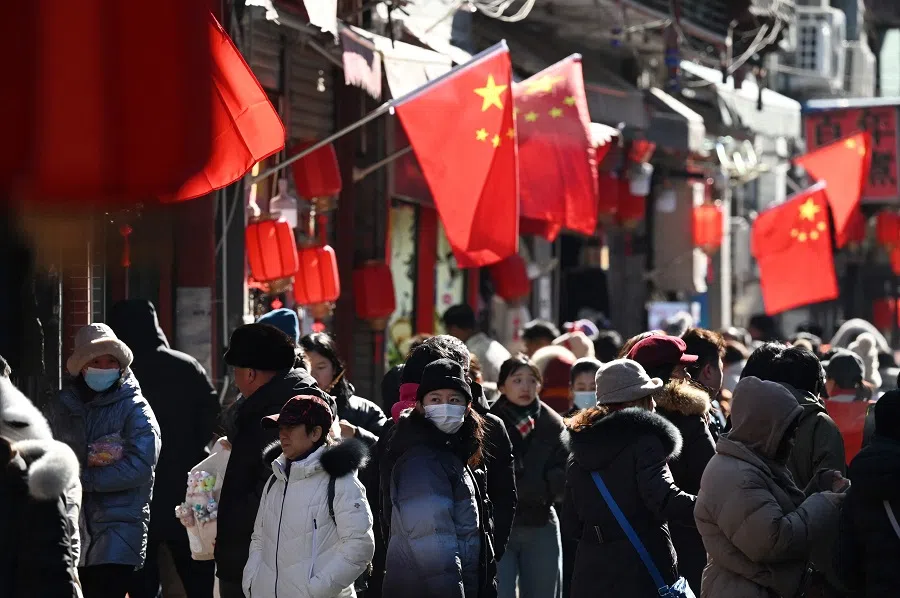People walk below Chinese flags in an alley near a popular shopping street on the sixth day of the Lunar New Year in Beijing on 3 February 2025. (Greg Baker/AFP)