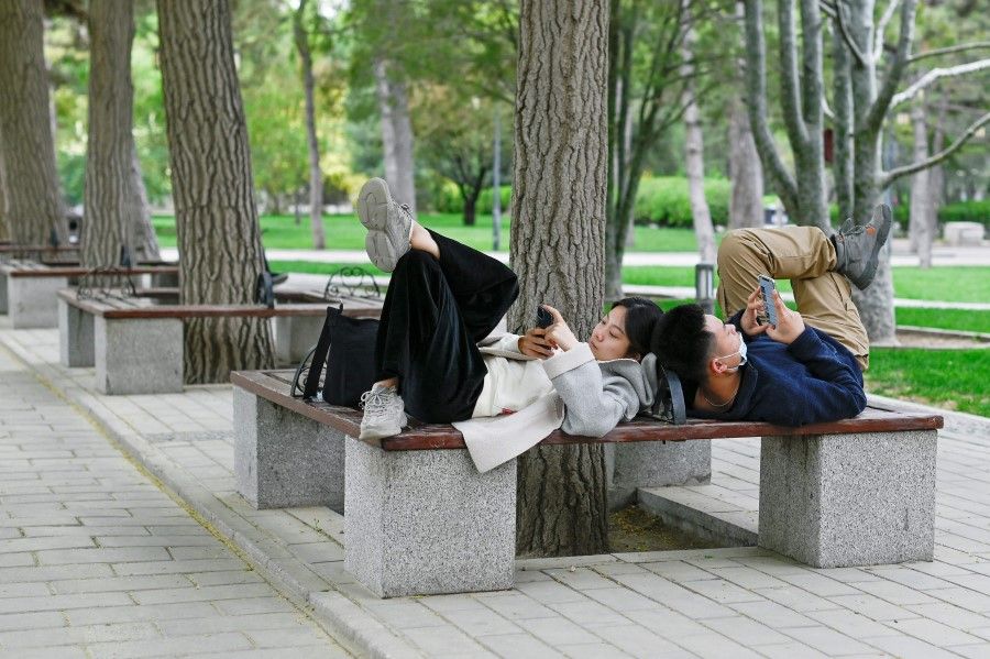 A couple use their mobile phones while sharing a bench at a park in Beijing on 21 April 2021. (Wang Zhao/AFP)