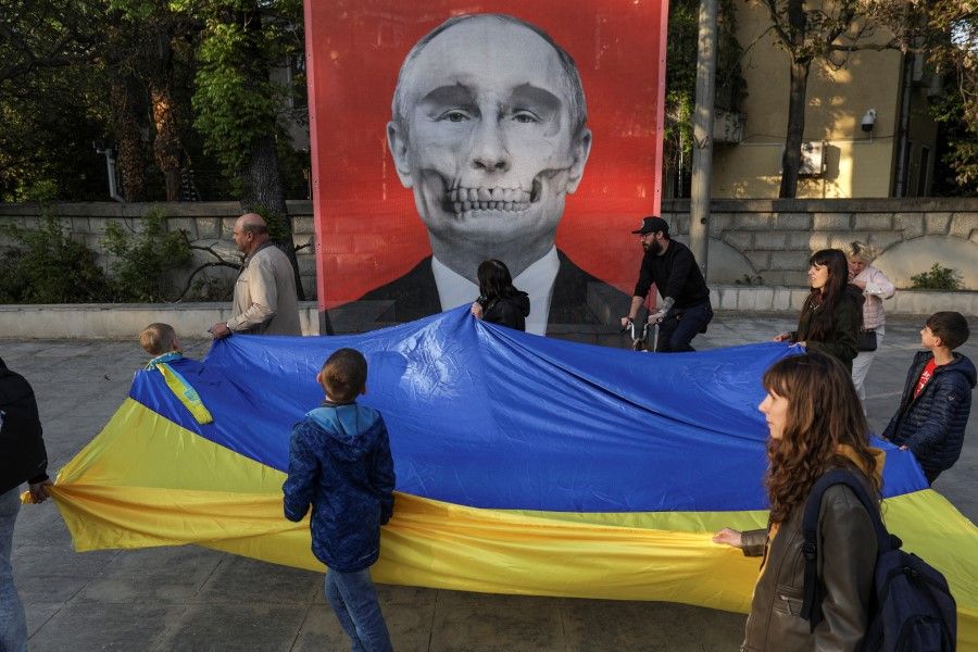 Protesters carrying a large Ukrainian flag and heading to a protest against Russia's war in Ukraine, walk by a mesh depicting an artistic view of Vladimir Putin's portrait, featured in an anti-war exhibition near the Russian Embassy, in Bucharest, Romania, 30 April 2022. (Octav Ganea via Reuters)