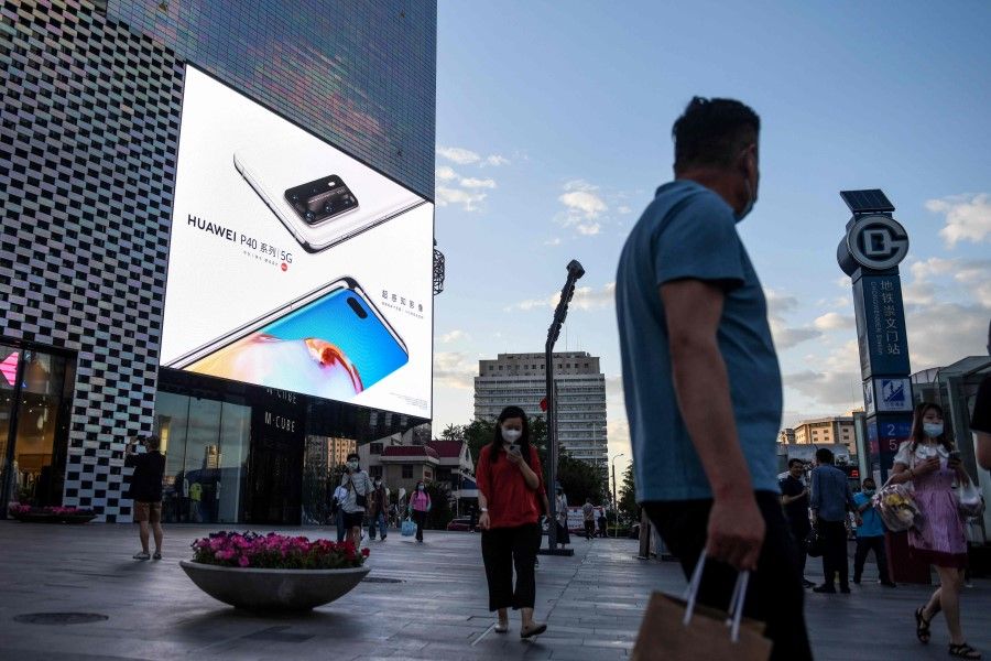 People walk past an advertisement for Huawei mobile phones on a mall in Beijing, 27 May 2020. (Greg Baker/AFP)