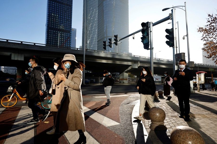 People walk across a street during morning rush hour, following the outbreak of the coronavirus disease (Covid-19), in the Central Business District (CBD) in Chaoyang District, Beijing, China, 21 November 2022. (Tingshu Wang/Reuters)