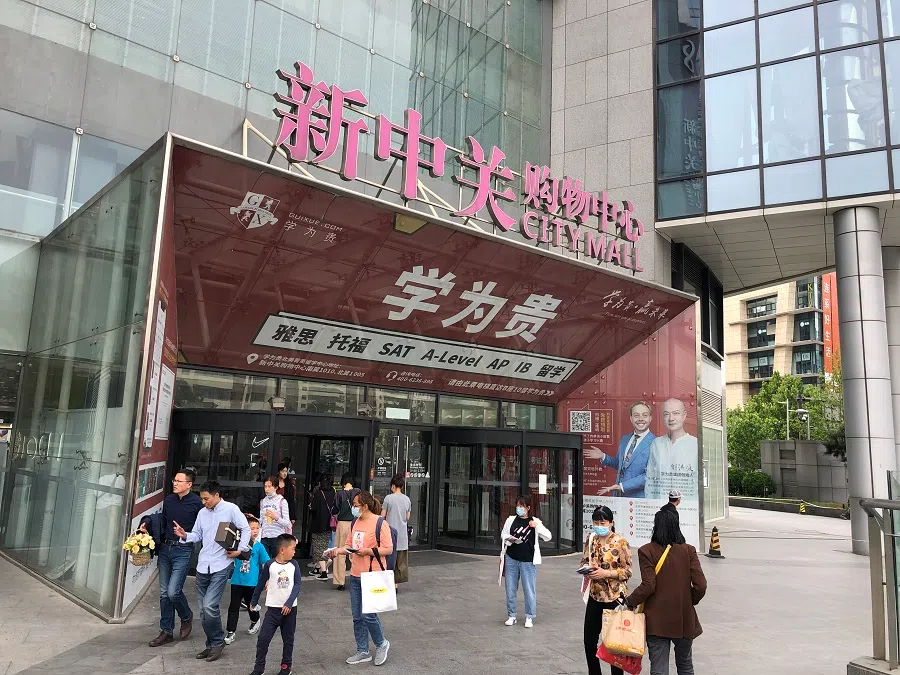 People outside a mall with an advertisement of an after-school institution plastered on the entrance.