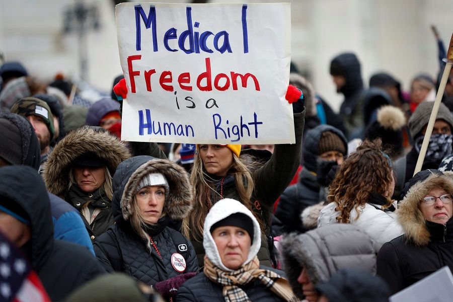 A woman holds a sign in the crowd as protestors demonstrate against Covid-19 vaccine mandates as they rally outside the New York State Capitol in Albany, New York, US, 5 January 2022. (Mike Segar/Reuters)