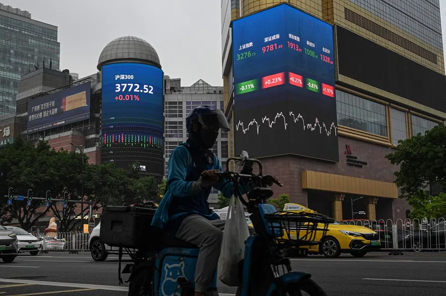 A delivery driver rides past screens showing stock market figures outside a shopping mall in Guangzhou, in southern China’s Guangdong province on 18 April 2025. (Jade Gao/AFP)