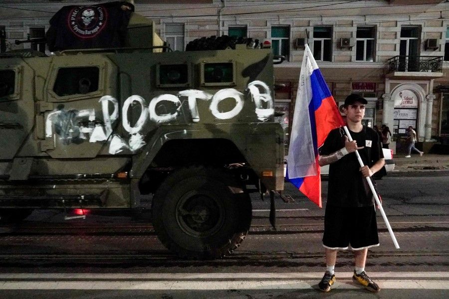A man holds the Russian national flag in front of a Wagner Group military vehicle in Rostov-on-Don late on 24 June 2023. (Stringer/AFP)