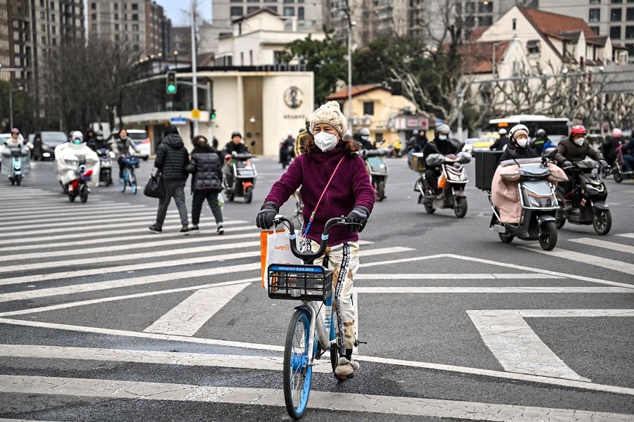 A woman crosses a street on a bicycle in the Jing'an district in Shanghai, China, on 22 February 2023. (Hector Retamal/AFP)