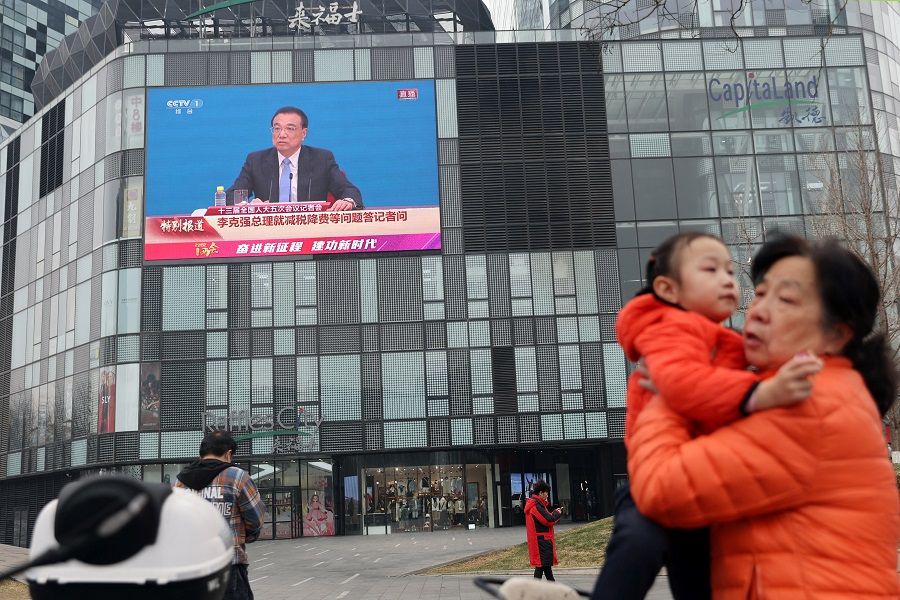 A woman holds a child near a giant screen showing a news conference by Chinese Premier Li Keqiang, following the closing session of the National People's Congress (NPC) at the Great Hall of the People in Beijing, China, 11 March 2022. (Tingshu Wang/Reuters)