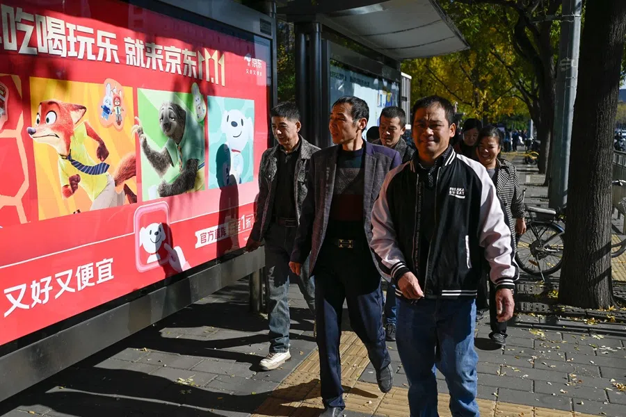 A group of people walk past a billboards promoting the "Double 11" online Shopping Festival at a bus stop in Beijing on 11 November 2025. (Wang Zhao/AFP)