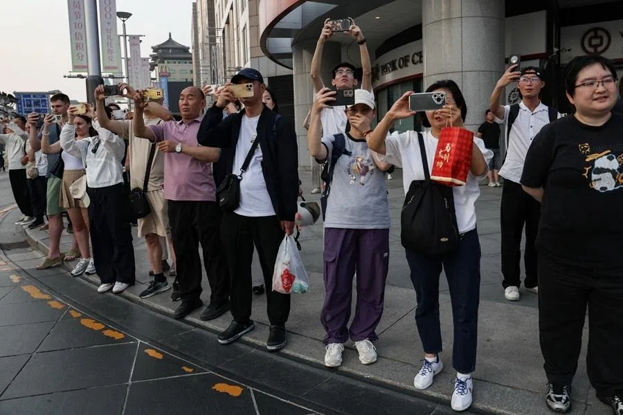 People use their phones as they watch a motorcade that is believed to be carrying US President Donald Trump travelling on Chang'an Avenue in Beijing, China, on 14 May 2026.