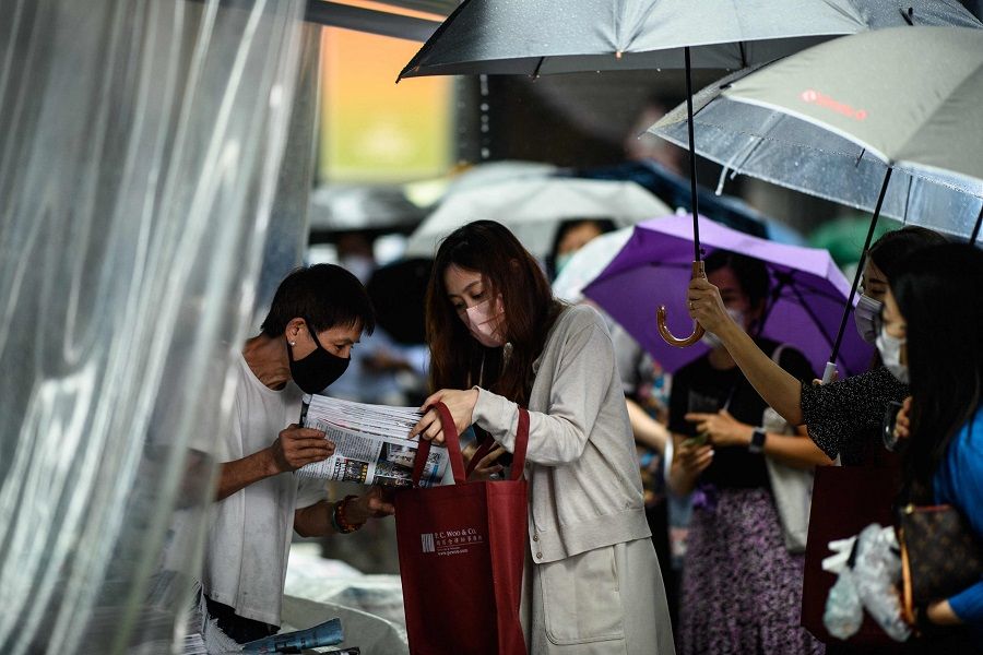 People hold umbrellas as a newsstand vendor (left) helps a customer protect her copy of the Apple Daily newspaper's final issue from the rain after she queued up to buy it from the street stall in Hong Kong, China on 24 June 2021. (Anthony Wallace/AFP)
