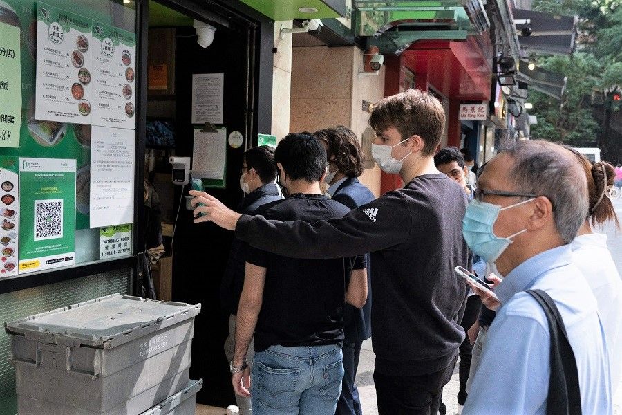 A man (centre) scans a QR code for the government's LeaveHomeSafe app, used for contact tracing amid the Covid-19 pandemic, to enter a restaurant in Hong Kong on 9 December 2021. (Bertha Wang/AFP)