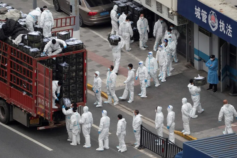 This photo taken on 5 April 2022 shows people wearing personal protective equipment as they transfer daily food supplies and necessities for local residents during the Covid-19 lockdown in Shanghai. (AFP)