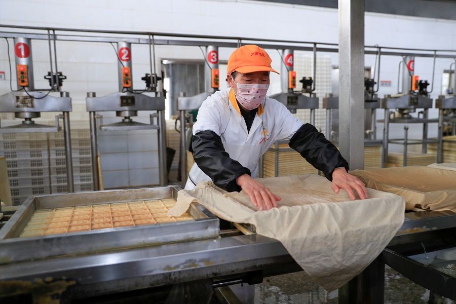 A worker wearing a face mask works on a production line manufacturing soybean-based food products at a factory in Hefei, Anhui, China, on 4 February 2020. Soybeans are most vulnerable to external factors but China's soybean supplies will not be affected with the signing of the China-US phase one trade agreement. (China Daily via Reuters)
