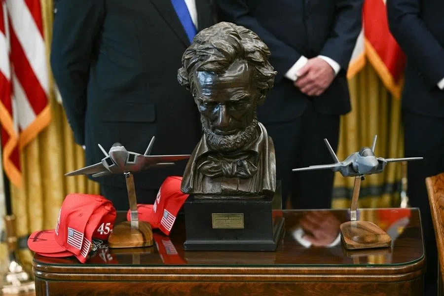 A stack of Donald Trump signed red "Make America Great Again" hats are seen on a table next to a bust of Abraham Lincoln during a meeting in the Oval Office at the White House in Washington, DC on 23 April 2026.