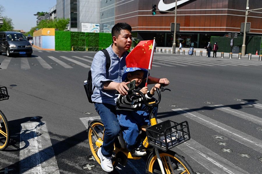 A man rides a sharing bicycle with a child along a business street in Beijing, China, on 18 April 2023. (Wang Zhao/AFP)