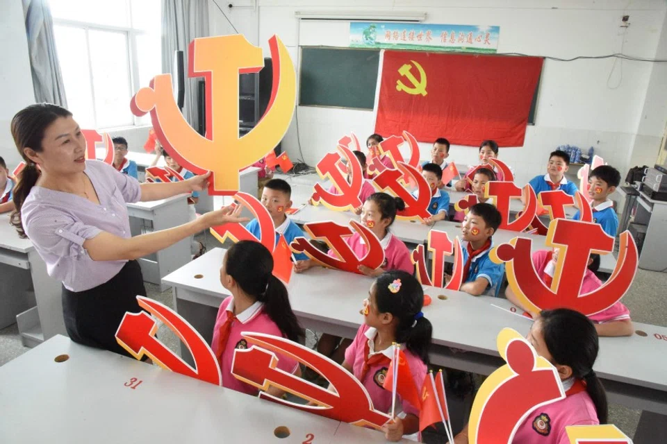 In this file photo a teacher and her students pose with Communist Party emblems during a class about the history of the Communist Party at a school in Lianyungang, in China's eastern Jiangsu province, 28 June 2020. (STR/AFP)