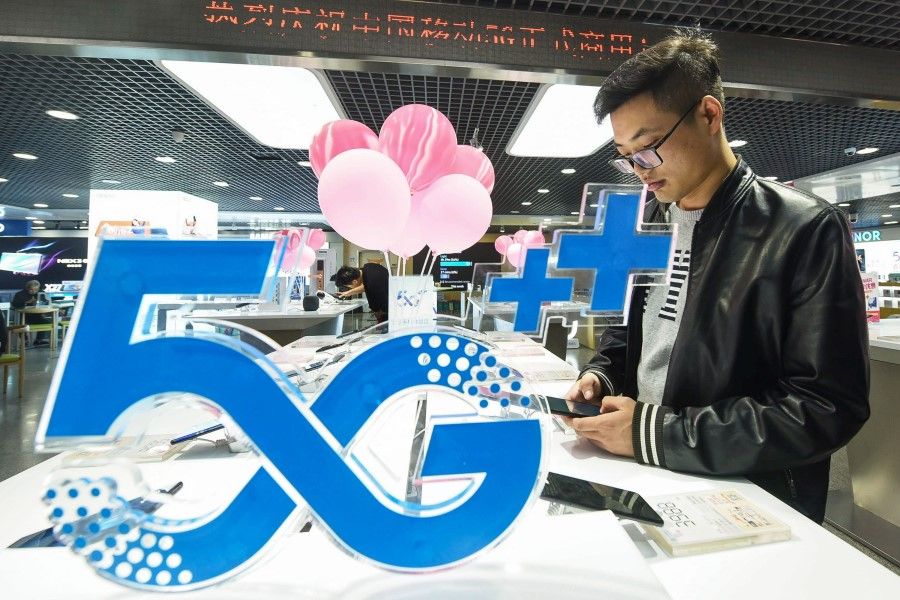 A customer looks at a mobile phone next to a 5G logo at a store in Hangzhou, October 2019. (AFP)