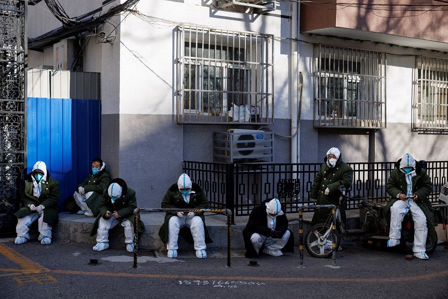 Pandemic control workers in protective suits sit in a neighbourhood that used to be under lockdown, in Beijing, China, 10 December 2022. (Thomas Peter/Reuters)