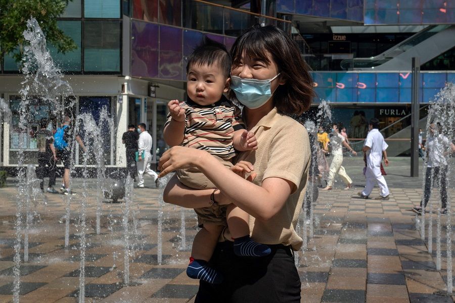 A woman holds her child outside a shopping mall in Beijing, China, on 1 June 2021. (Nicolas Asfouri/AFP)